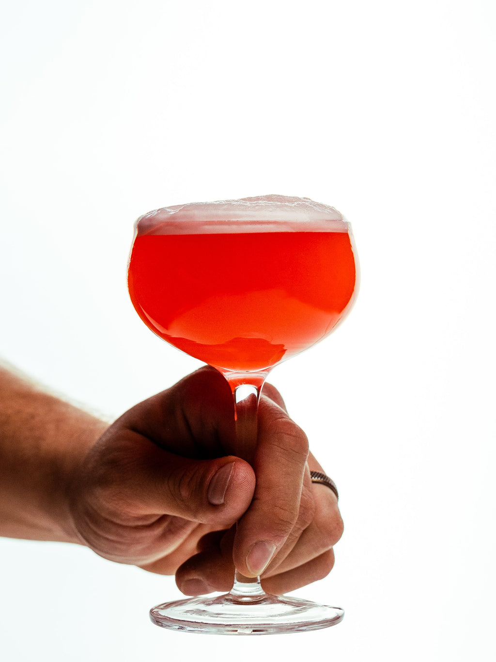 Hand holding a red cocktail in a glass with a white background