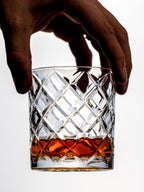Hand holding a crystal glass filled with whiskey on a white background