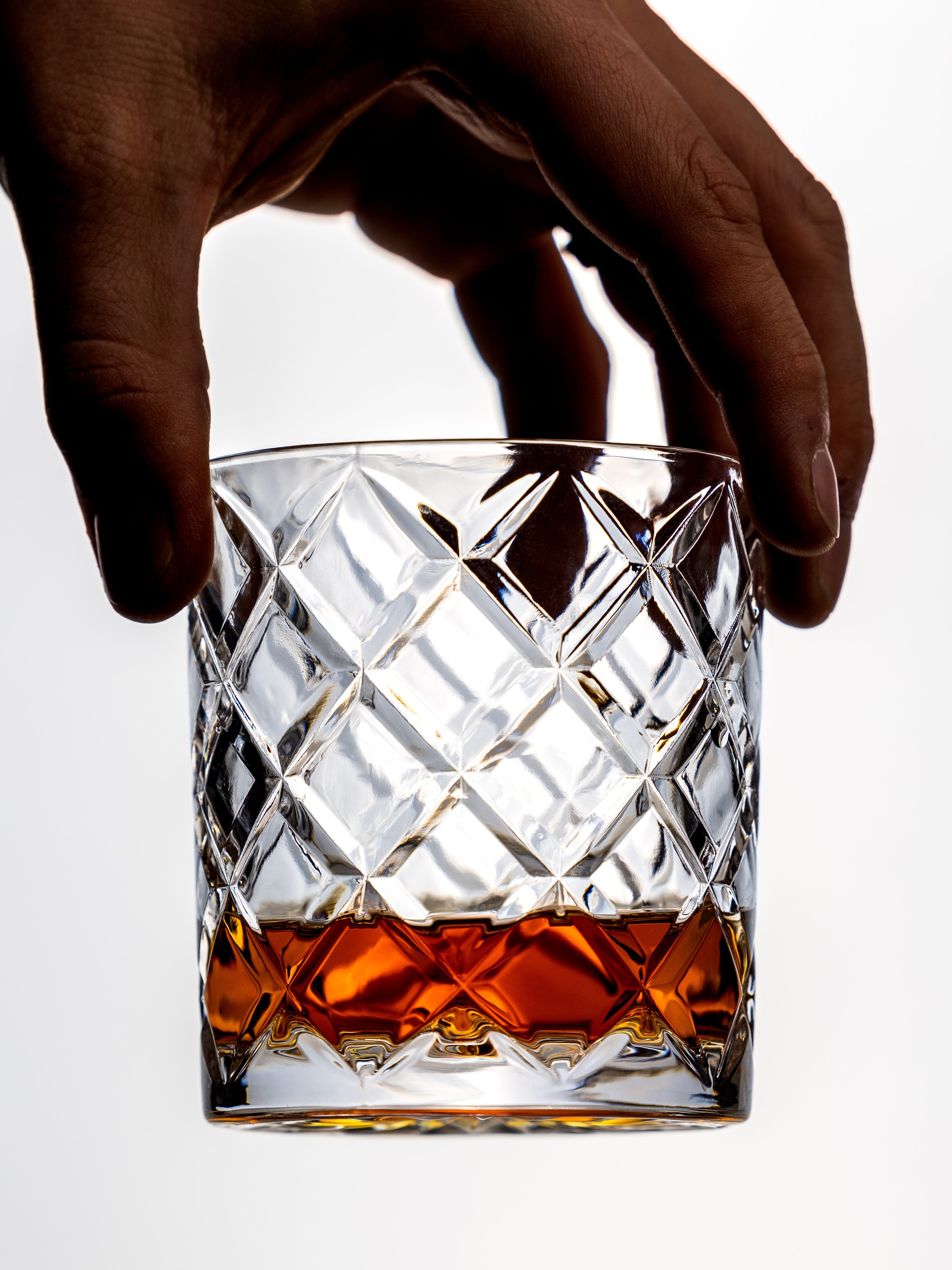 Hand holding a crystal glass filled with whiskey on a white background