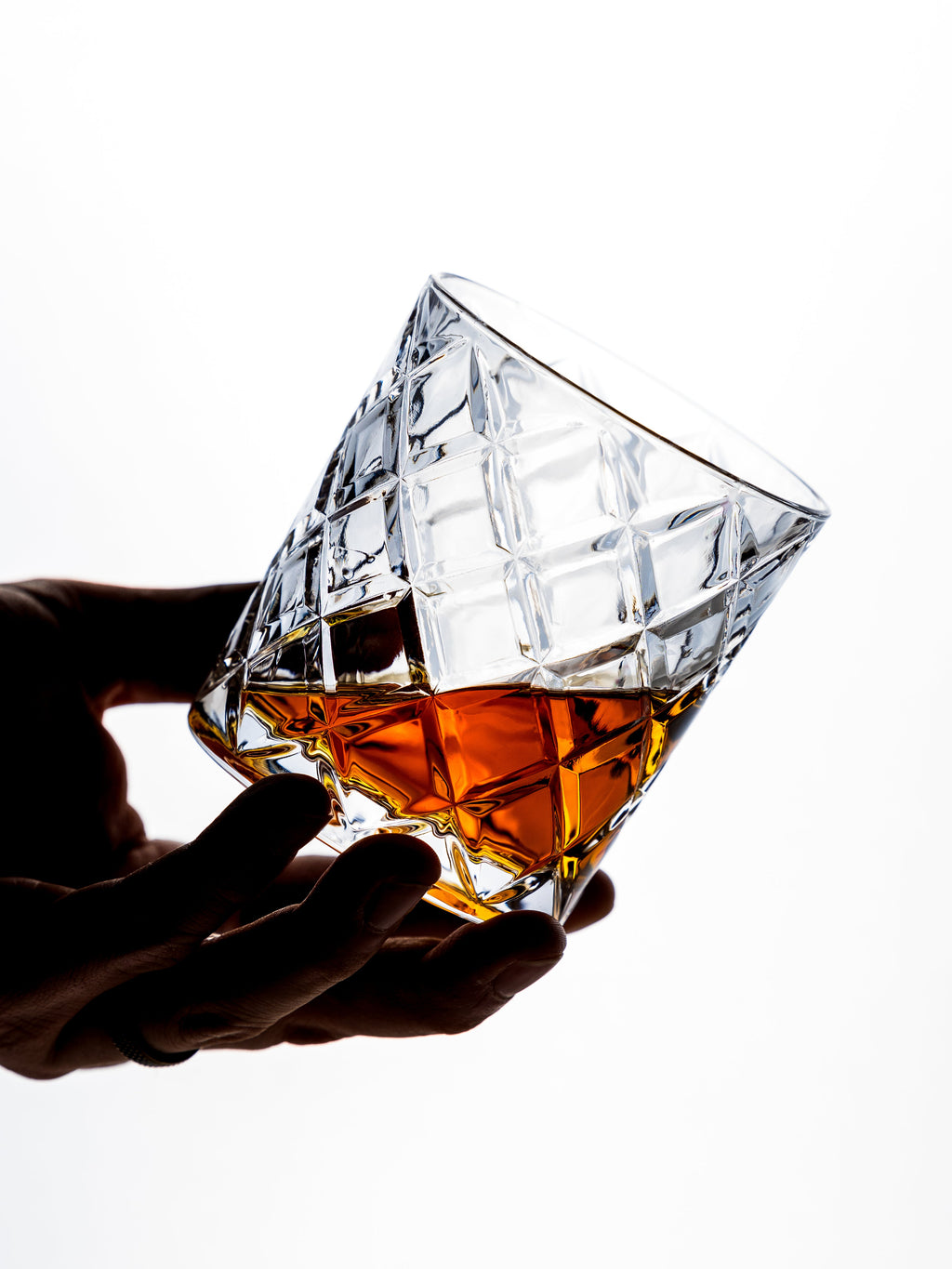 Hand holding a diamond-shaped crystal glass filled with amber liquid on a white background