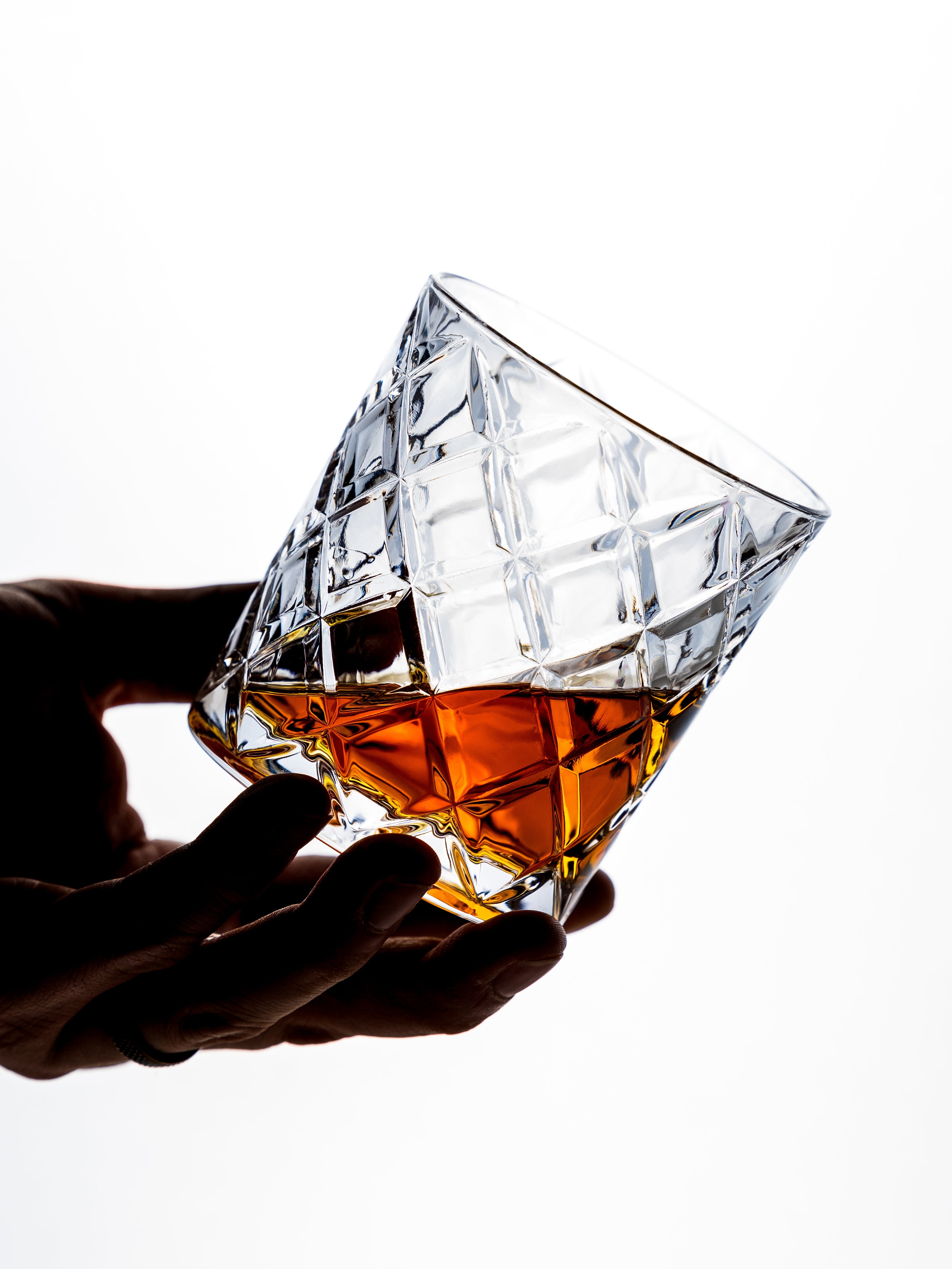 Hand holding a diamond-shaped crystal glass filled with amber liquid on a white background