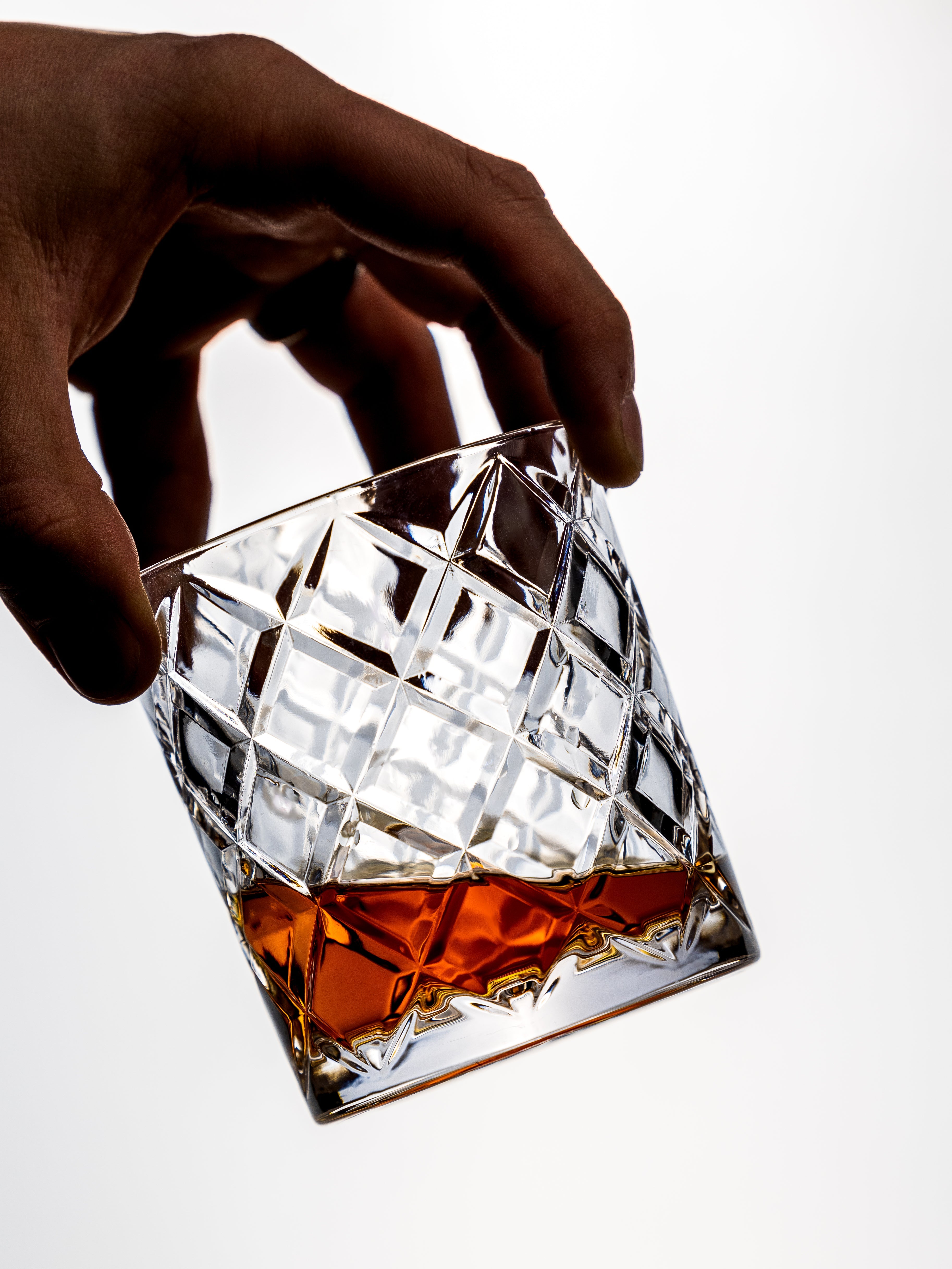 Hand holding a crystal glass with a drink on a white background