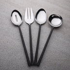 Set of black-handled silverware including a fork, two spoons, and a ladle on a gray surface.