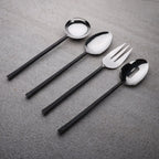 Set of black-handled silverware including a fork, two spoons, and a knife on a gray surface.