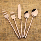 Set of rose gold cutlery including forks, knives, and spoons on a textured beige background.