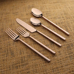 Set of silver cutlery including a knife, fork, and two spoons on a textured brown surface.