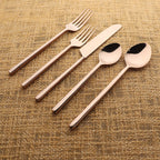 Set of rose gold cutlery including fork, knife, and two spoons on a textured fabric background.