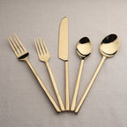 Set of gold-plated cutlery including two forks, a knife, and two spoons on a gray background.