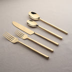 Set of gold cutlery including knife, forks, and two spoons on a gray background