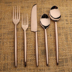 Set of bronze cutlery including forks, knives, and spoons on a textured fabric background.