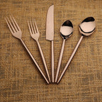 Set of rose gold cutlery including forks, a knife, and spoons on a textured brown background.