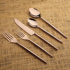 Set of bronze cutlery including a knife, two spoons, and two forks on a textured brown fabric background.