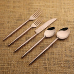 Set of bronze cutlery including forks, knives, and spoons on a textured brown background.