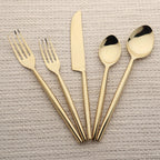Set of gold cutlery including forks, a knife, and spoons on a textured surface.