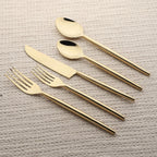 Set of gold cutlery including knife, fork, and two spoons on a textured surface.