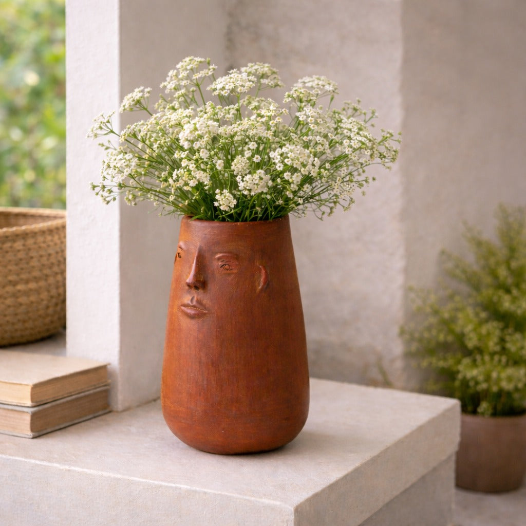 Ceramic vase with face design containing white flowers on a surface.