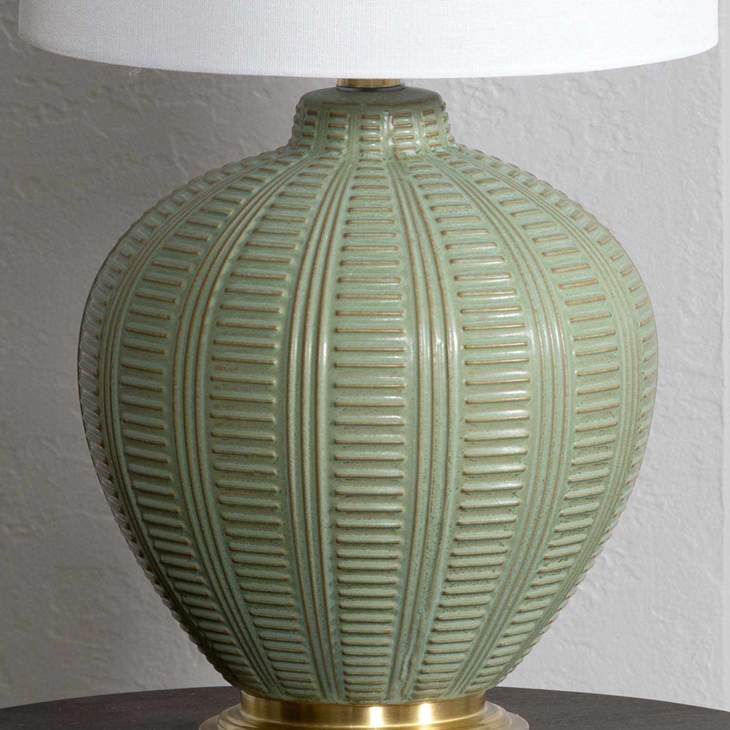 Green textured table lamp with a white lampshade on a neutral background