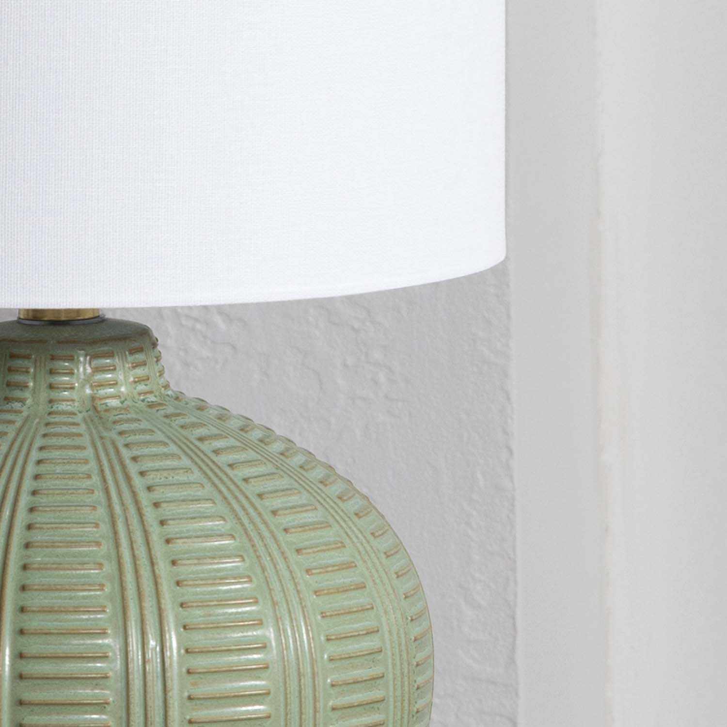 Close-up of a textured green lamp base with a white lampshade against a light gray background