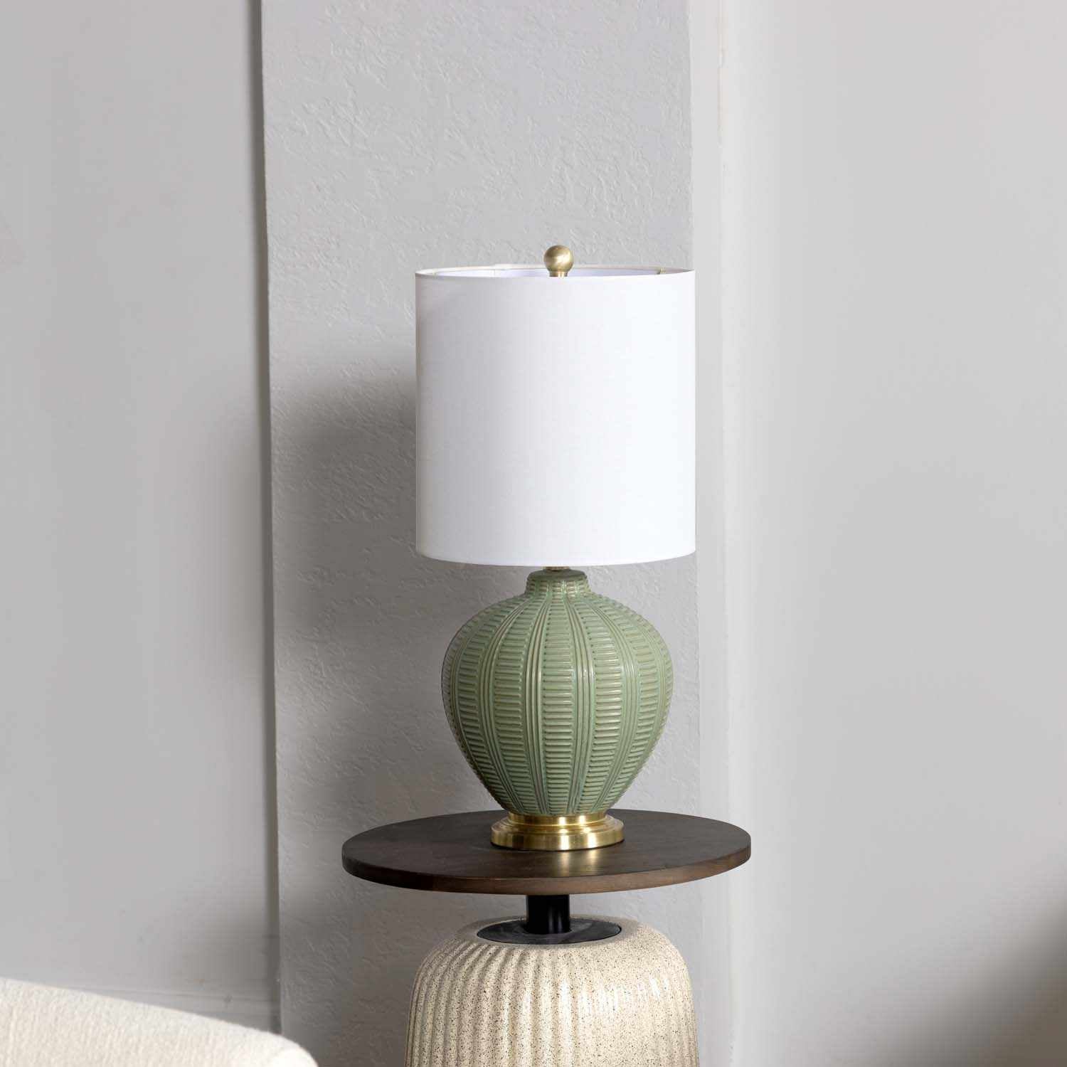 Green textured table lamp with white shade on a wooden side table against a gray wall.
