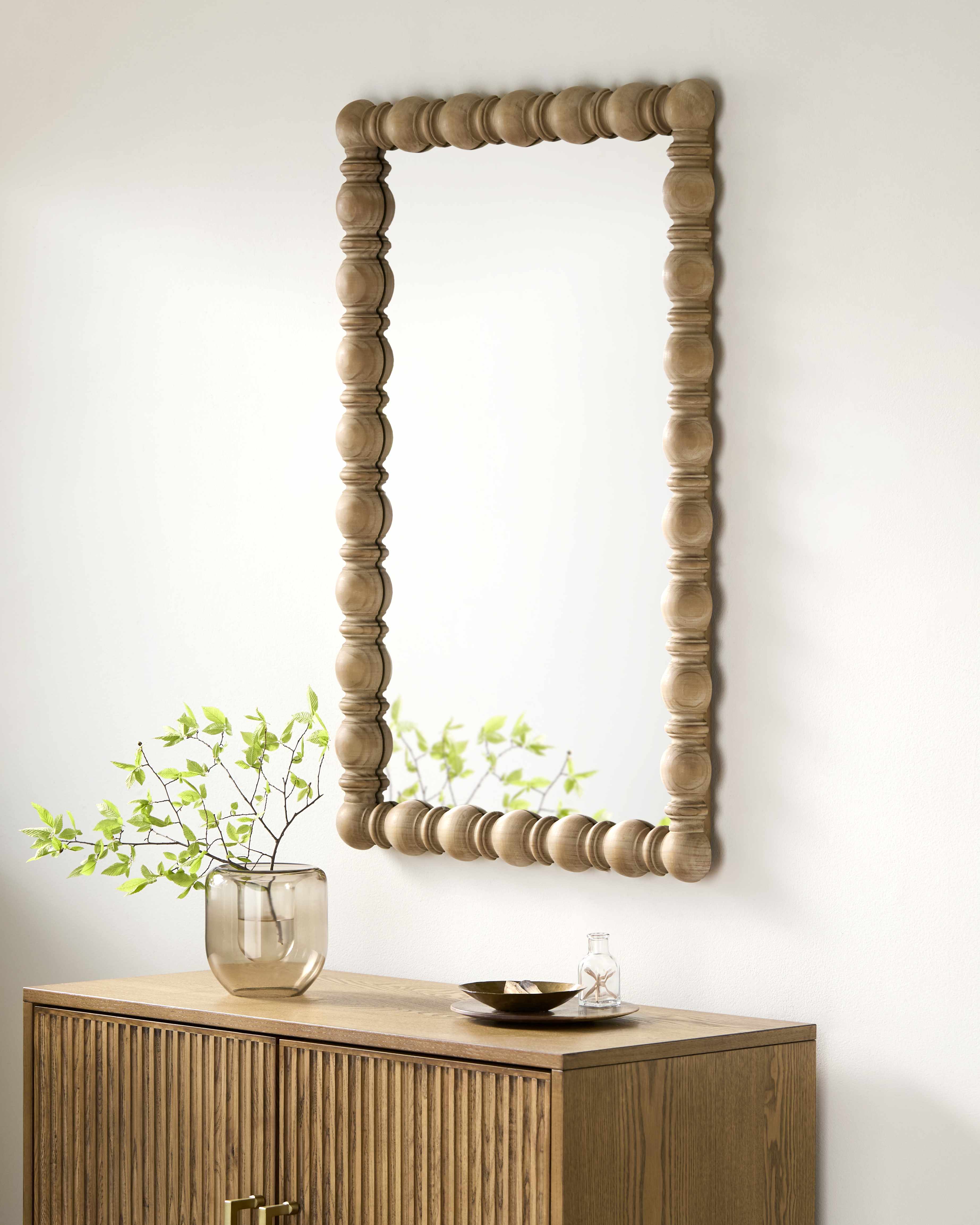 Wooden mirror on a white wall above a wooden cabinet.