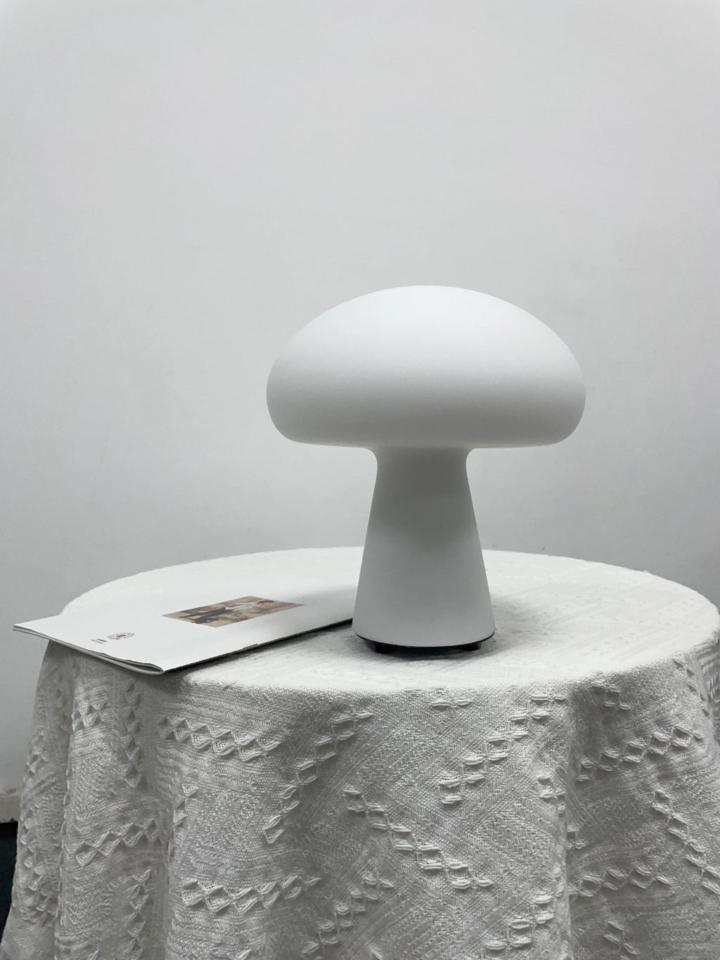White mushroom-shaped lamp on a textured white surface with a light gray background