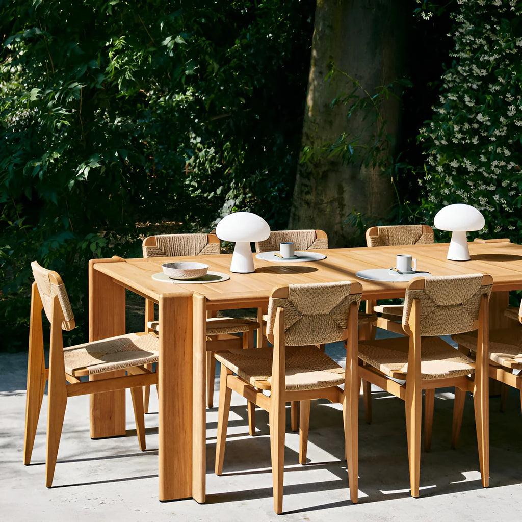 Wooden outdoor dining table with chairs and table lamps in a garden setting