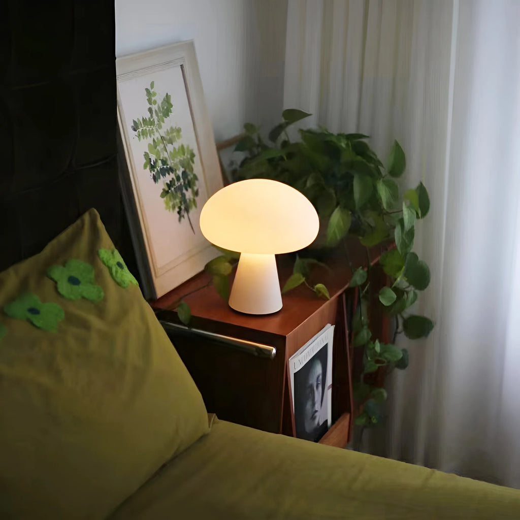 Lamp on a nightstand next to a bed with green pillows and a plant in the background