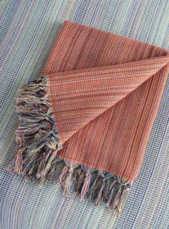 Folded orange king size blanket with multicolor fringe on textured surface