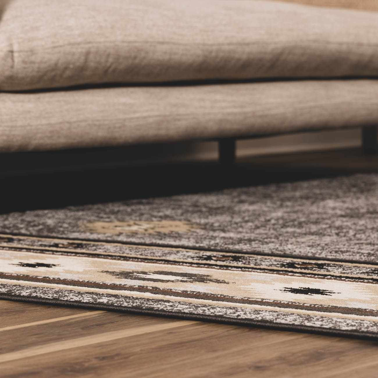 Close-up of a textured rug on a wooden floor with a blurred sofa in the background.