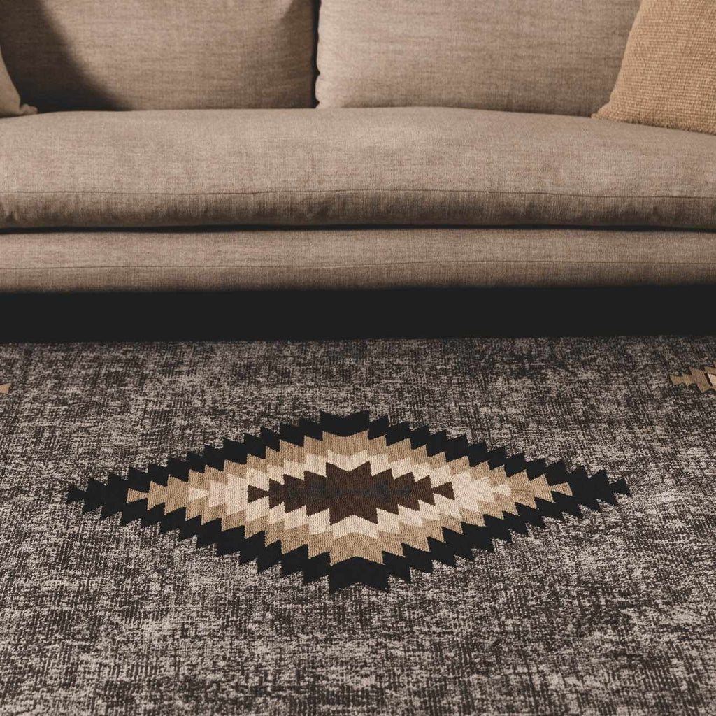 Geometric patterned rug on a textured floor with a brown sofa in the background