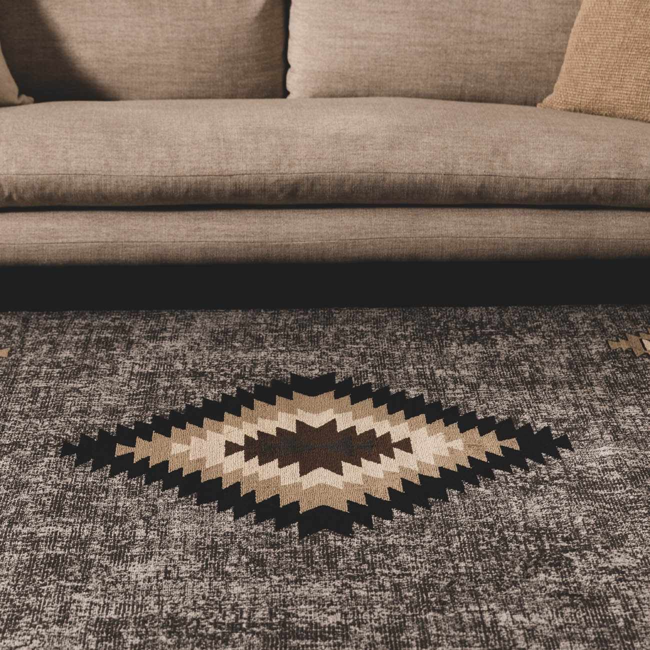 Geometric patterned rug on a textured floor with a brown sofa in the background