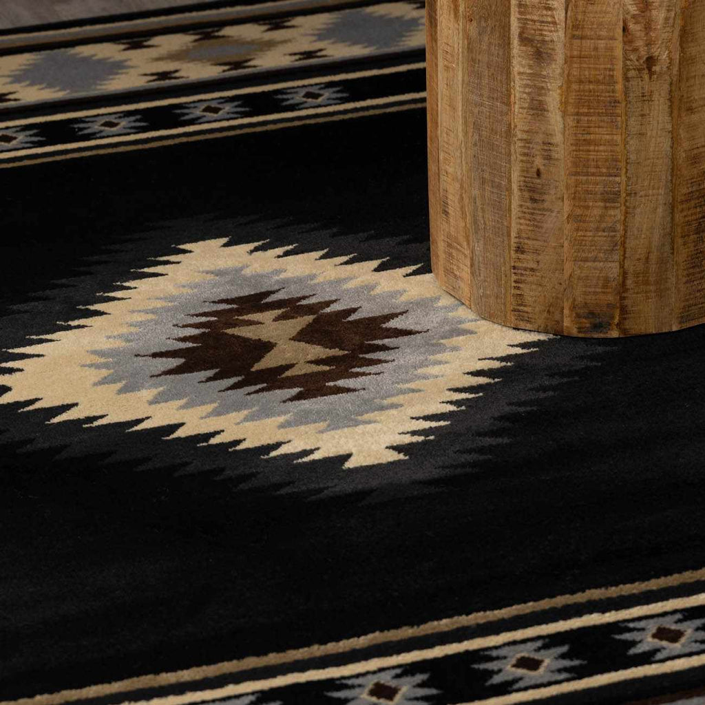 Close-up of a patterned rug with geometric design on a dark floor.