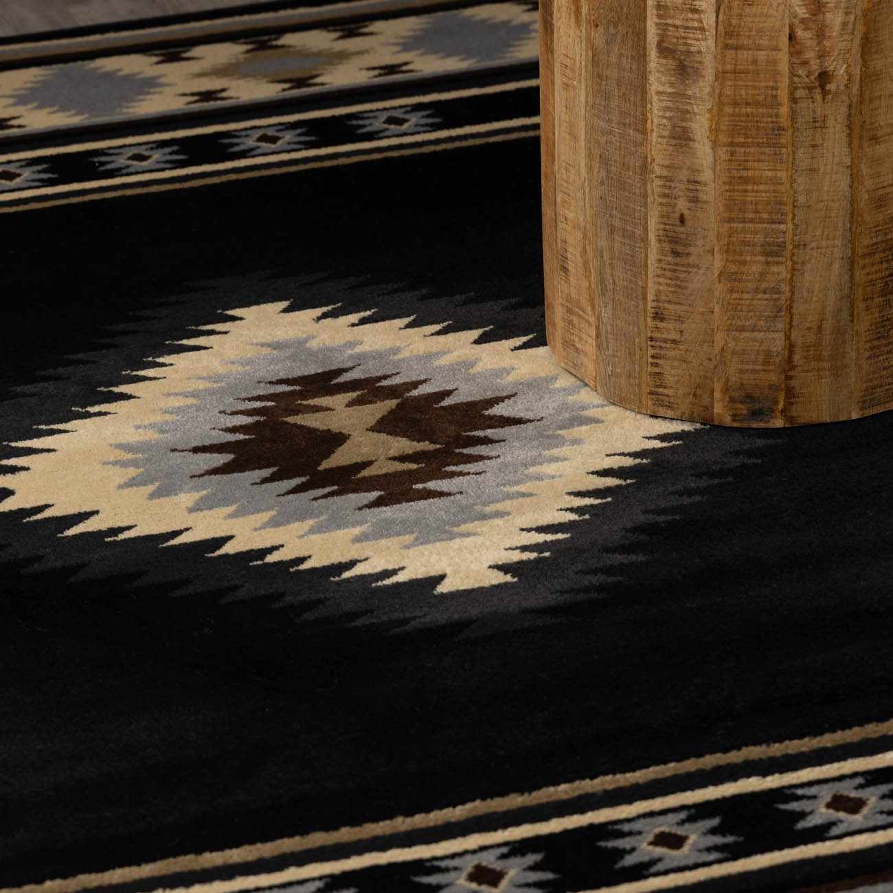 Close-up of a patterned rug with geometric design on a dark floor.