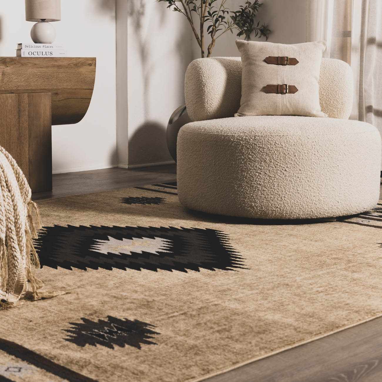 Beige armchair with a patterned pillow on a textured rug in a room with wooden furniture and decor.