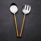 Two spoons, one with a round bowl and gold handle, the other with a slotted design and gold handle, on a dark background.