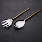 Silver salad servers with wooden handles on a dark gray background