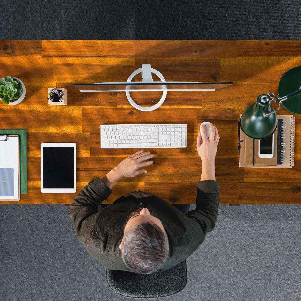Person using a computer at a wooden desk with various items.