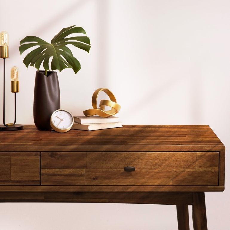 Wooden desk with decorative items including a plant, clock, and books on a plain background