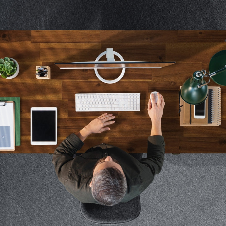 Person using a computer at a wooden desk with various items.