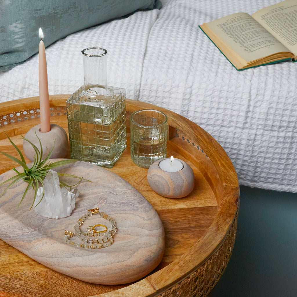Wooden tray with decorative items including a candle, glass, and jewelry on a couch.