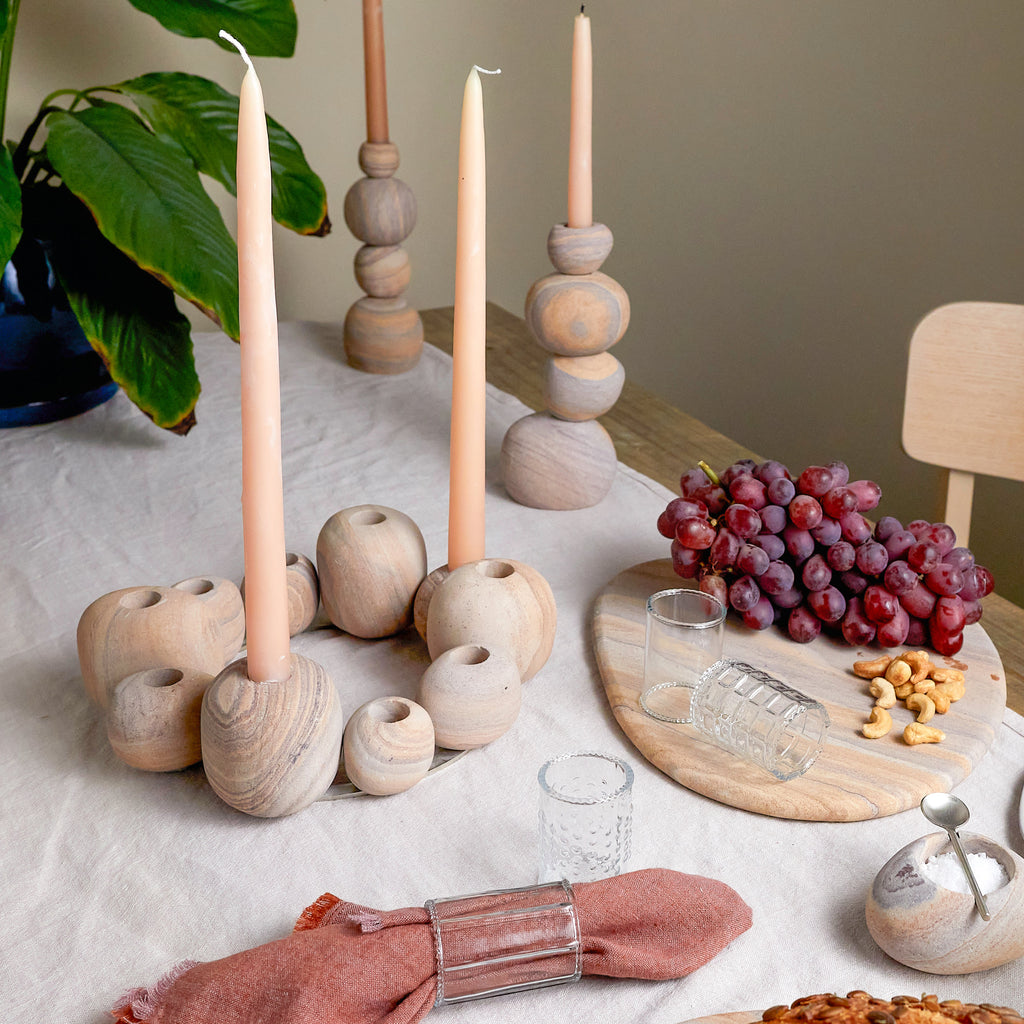Decorative table setting with wooden candle holders, candles, grapes, and a glass on a light surface.