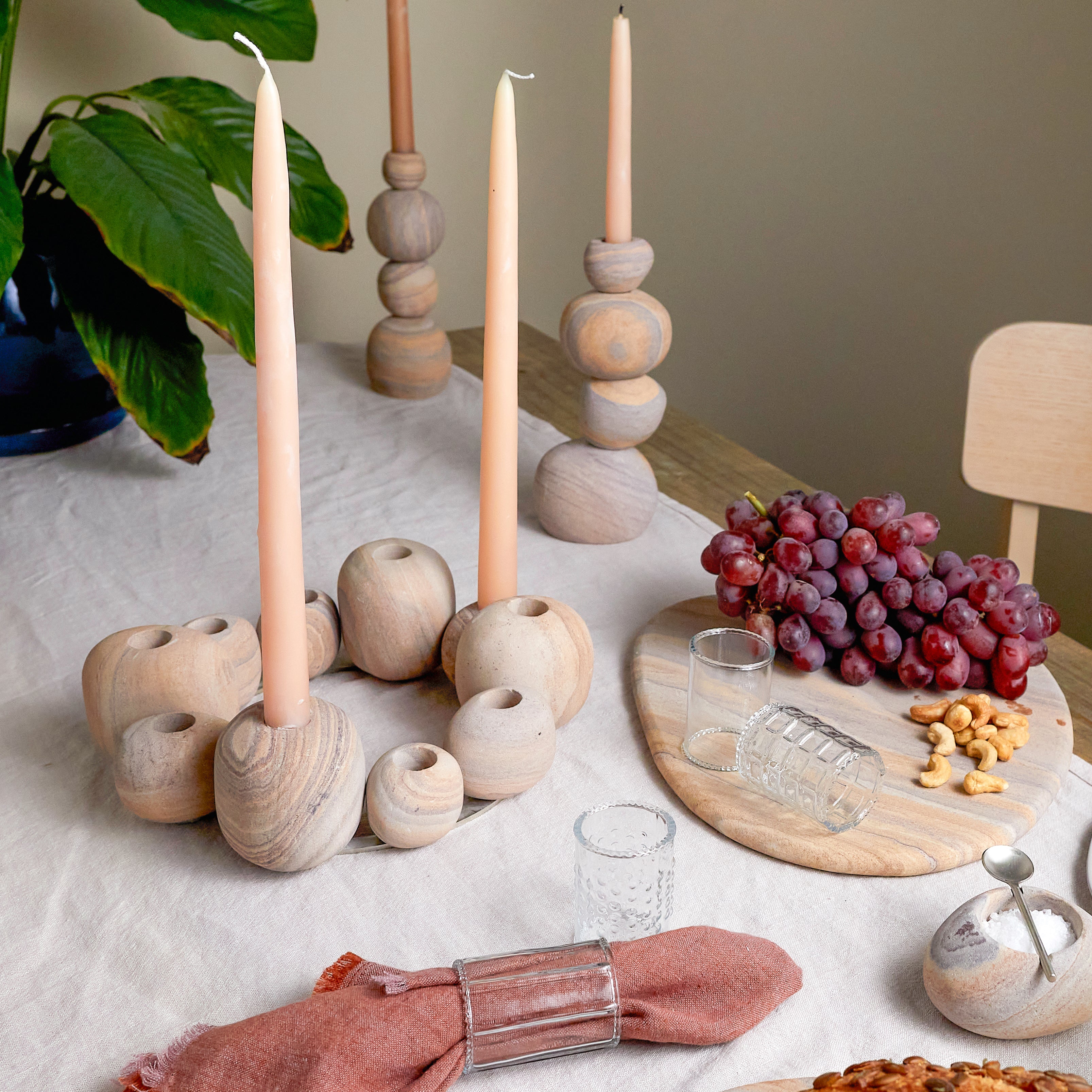 Decorative table setting with wooden candle holders, candles, grapes, and a glass on a light surface.
