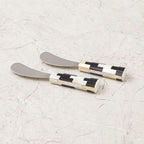 Two butter knives with checkered handles on a light gray surface