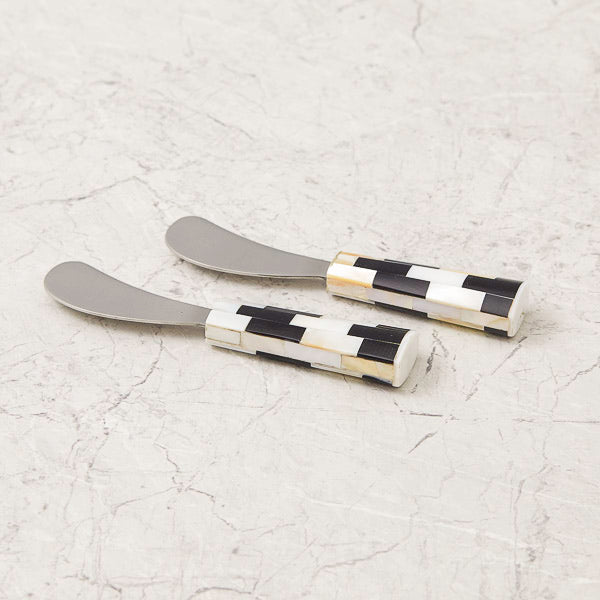 Two butter knives with checkered handles on a light gray surface