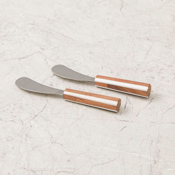 Two metal spreaders with wooden handles on a light gray textured surface