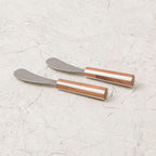 Two metal spreaders with wooden handles on a light gray textured surface