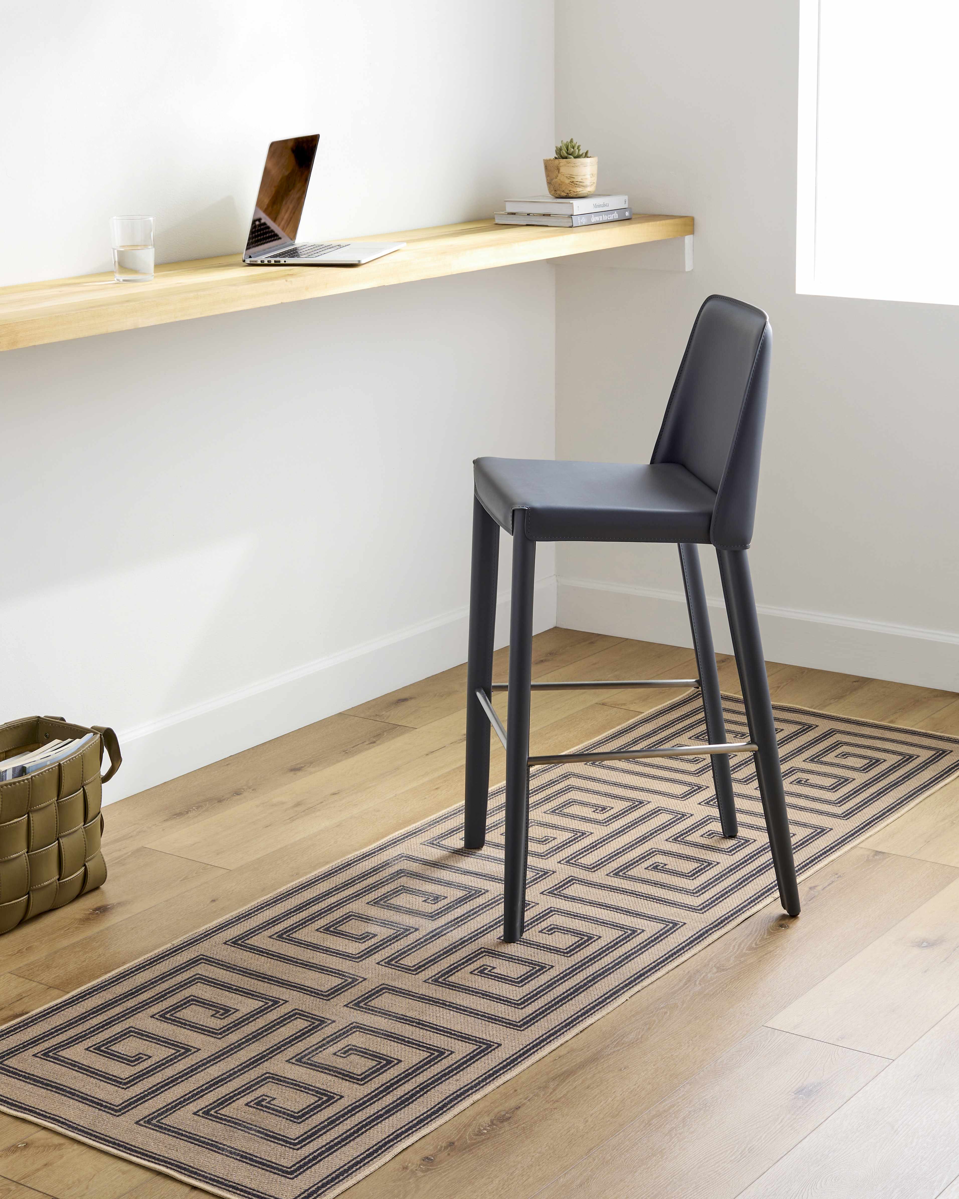 Black bar stool in a room with a wooden desk and geometric rug
