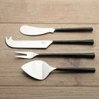 Set of four cheese tools with black handles on a wooden surface