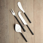 Set of four black-handled silver cheese utensils on a wooden surface