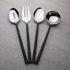 Set of black-handled silverware including a fork, two spoons, and a ladle on a gray surface.